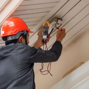 A certified Electrician Level 2 Sydney wearing a safety helmet while testing an electrical connection on a ceiling using a clamp meter.