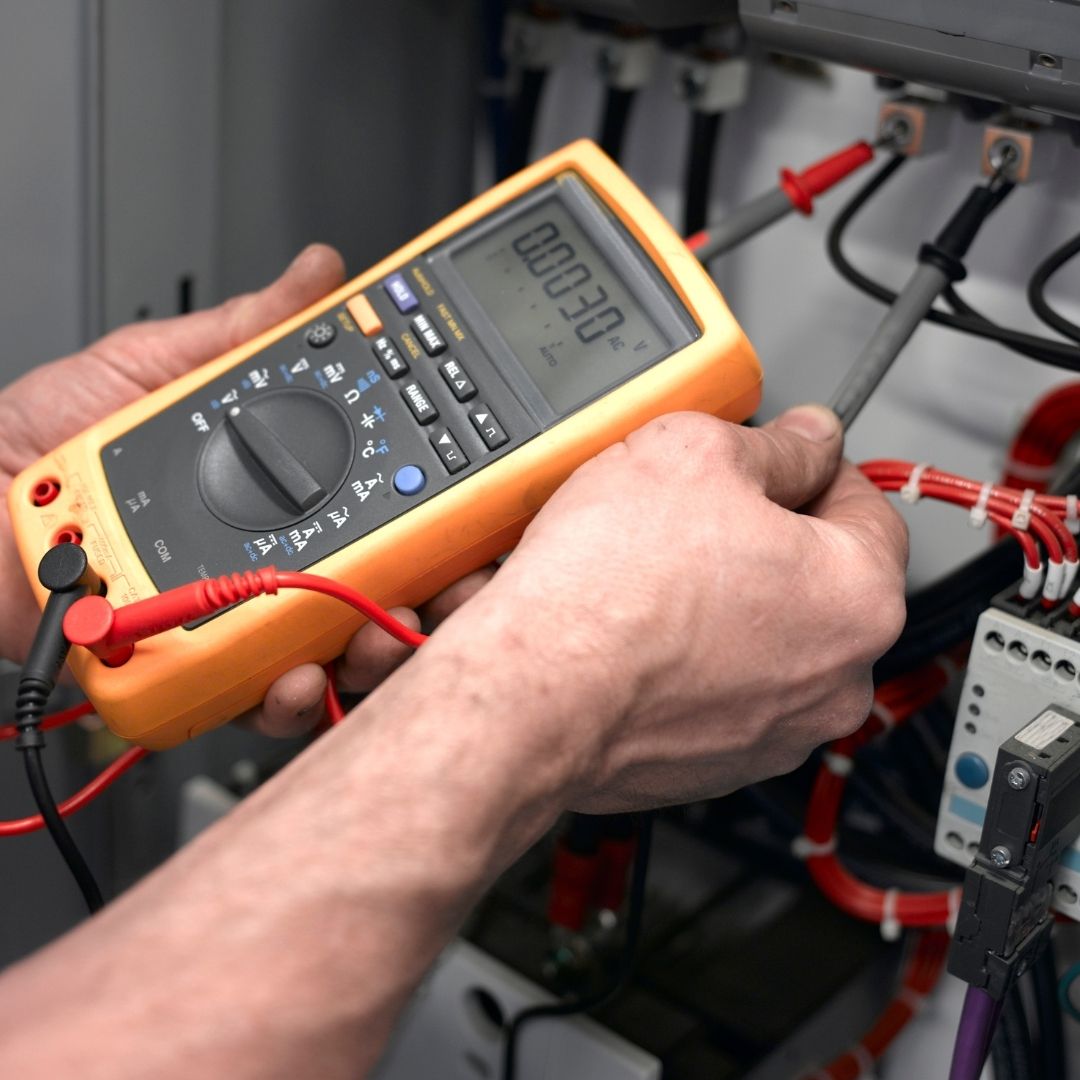A professional electrician conducting an electrical test house inspection using a digital multimeter to measure voltage and ensure safe circuit performance in an electrical panel.