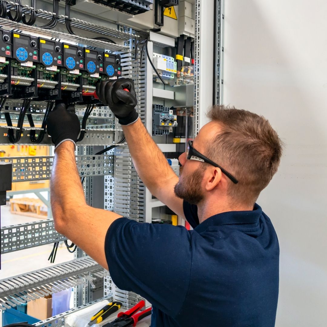 A skilled Electrician Balmain East wearing safety glasses and gloves, using a screwdriver to install and configure an industrial electrical panel in a commercial setting.