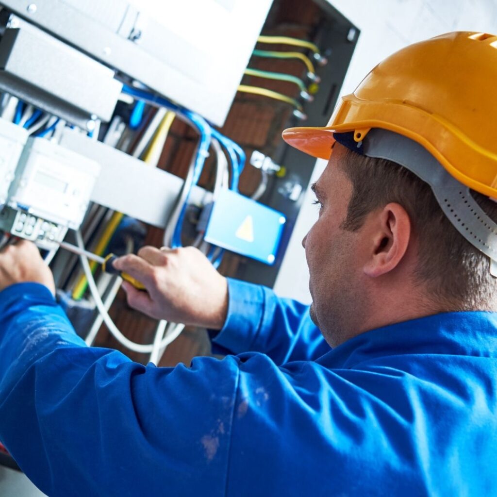 A professional electrician wearing a safety helmet and blue uniform performing data cable installation, ensuring proper wiring and secure network connectivity.