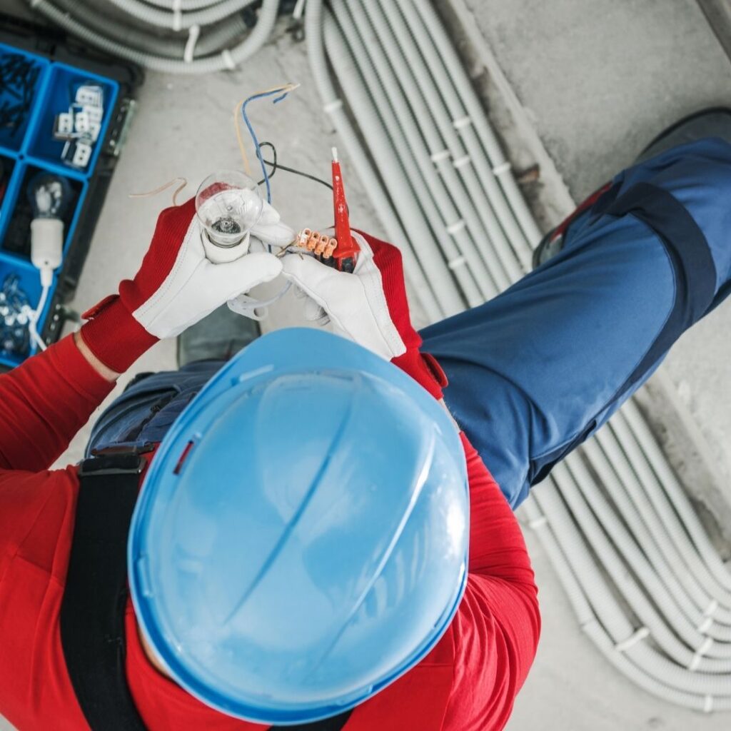 A commercial electrician in safety gear working on a light fixture, ensuring proper wiring and installation—showcasing the expertise of Commercial Electrical Contractors Sydney.