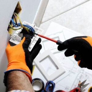 A professional Domestic Electrician wearing safety gloves installs a wall socket, ensuring proper wiring and secure connections for safe home electrical systems.