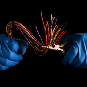 A Domestic Electrician in Sydney wearing protective gloves skillfully handles multiple colorful electrical wires using pliers, ensuring safe and precise wiring.