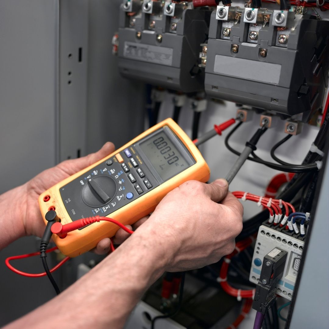 An electrician using a digital multimeter for testing wiring in an industrial electrical panel, ensuring proper voltage levels and system safety.