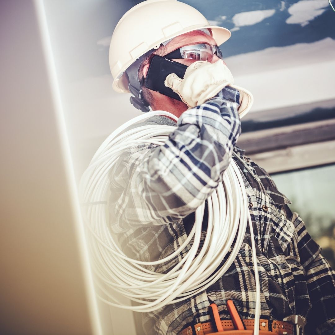 A licensed electrician in Sydney wearing protective gear while carrying electrical wiring and taking a work call, ensuring smooth communication and project efficiency.