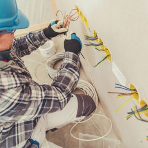 A professional Electrician Level 2 Sydney wearing protective gloves and a blue helmet, carefully organizing and installing electrical wiring into multiple wall outlets.