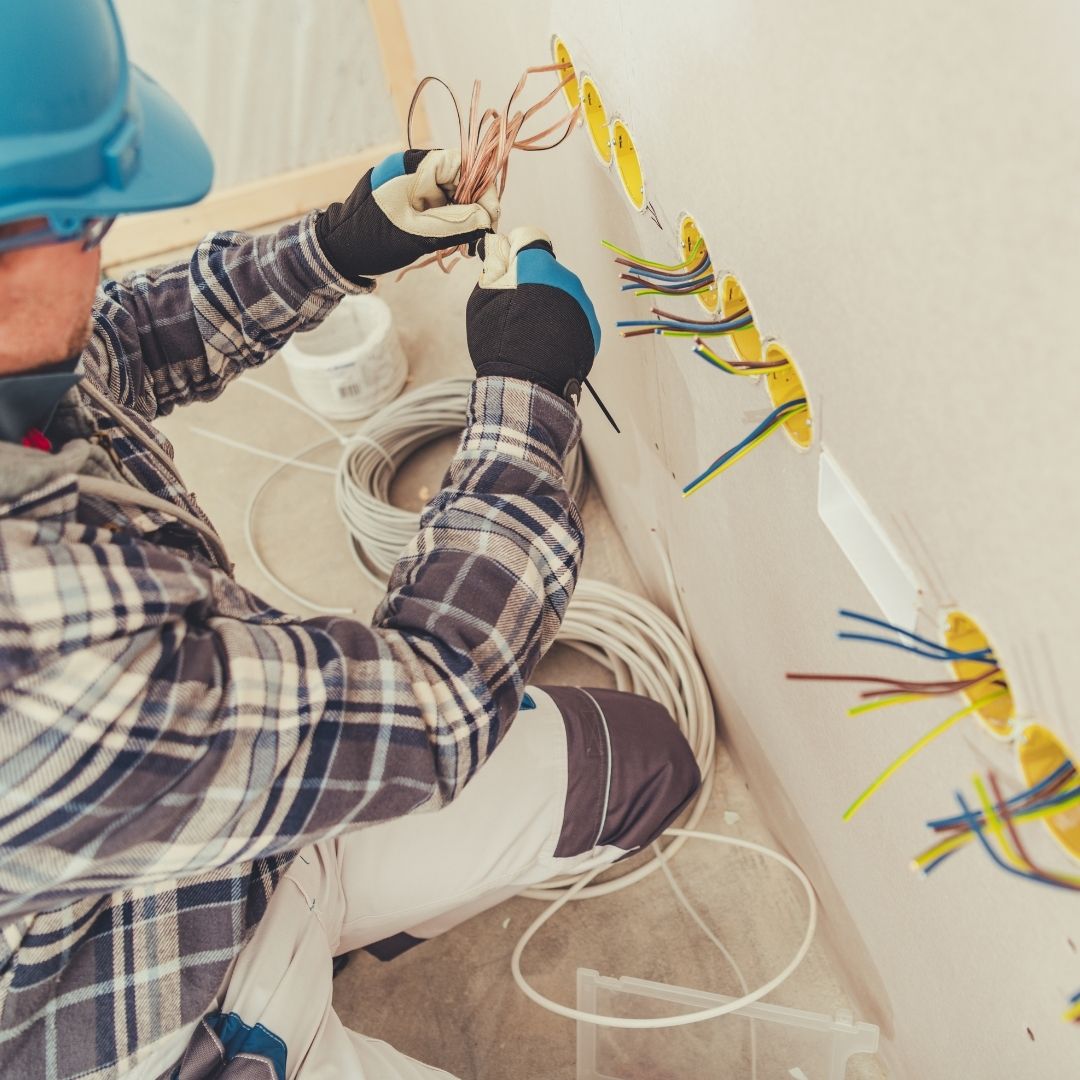 A professional Electrician Level 2 Sydney wearing protective gloves and a blue helmet, carefully organizing and installing electrical wiring into multiple wall outlets.