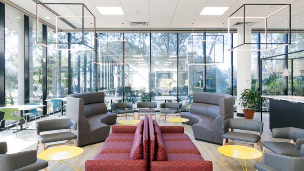 Modern office fitouts in Sydney featuring open lounge seating, glass walls, and stylish lighting design for collaborative spaces.