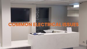 A sleek, minimalist office reception area showcasing integrated technology (a large mounted screen) and access to a meeting room. The text overlay, "COMMON ELECTRICAL ISSUES", directly warns of potential power and technology electrical problems in a corporate environment. This promotes the specialized knowledge of a commercial electrician required to maintain such demanding systems.