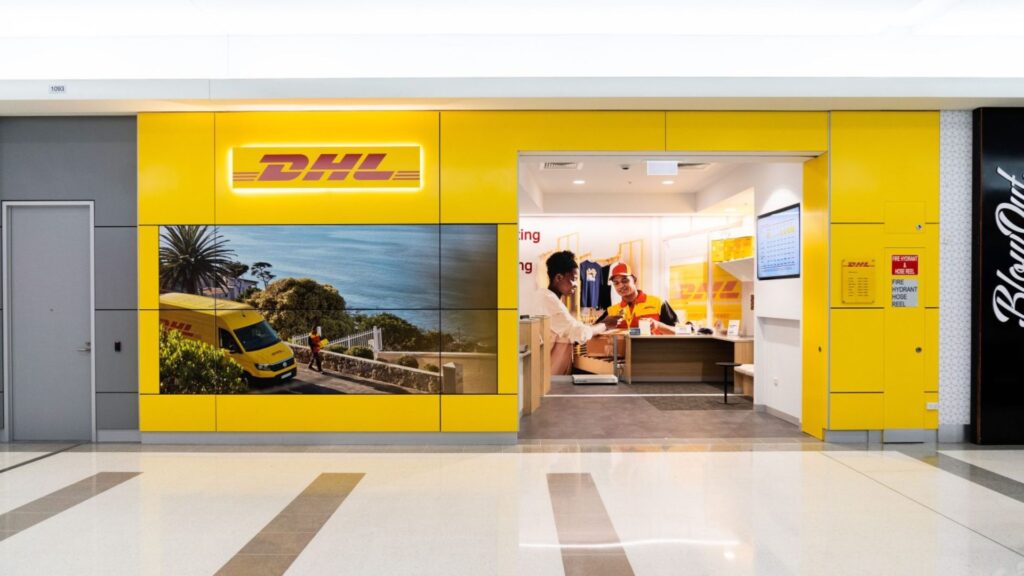 A striking image of a modern, brightly lit DHL service center in a mall environment. The extensive use of integrated lighting, video walls, and the high-power demand of a commercial retail operation underscores the necessity of hiring the best commercial electrician to ensure uninterrupted and aesthetically pleasing electrical infrastructure.