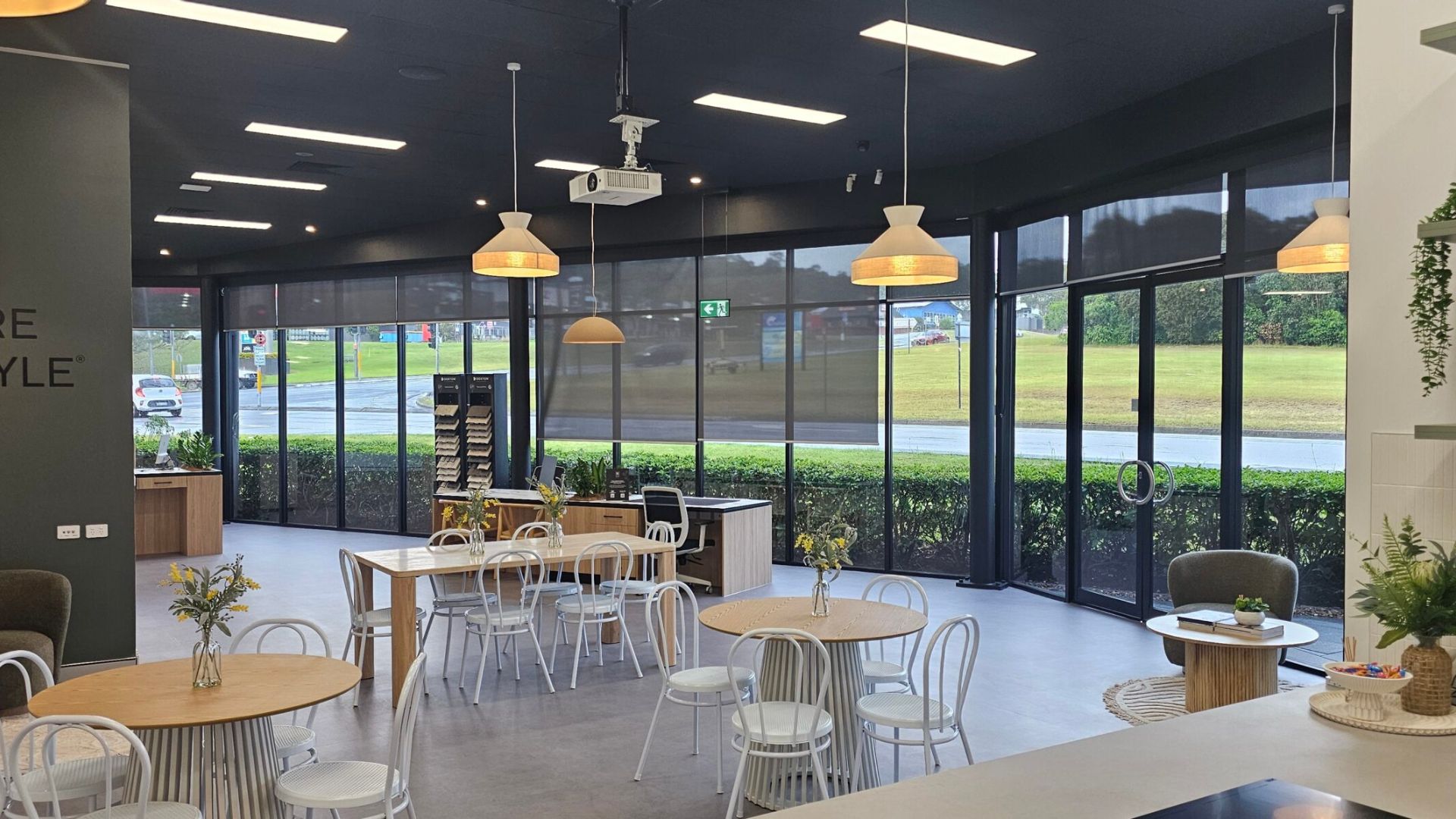 A modern office breakout area with several round tables and stylish white pendant lights installed by an office fit-out electrician in Sydney.