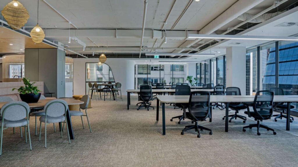 Open-plan commercial office floor with suspended linear LED lights and ergonomic workstations, demonstrating commercial fit-out services in a commercial vs industrial electrician comparison, by Lightspeed Electrical.