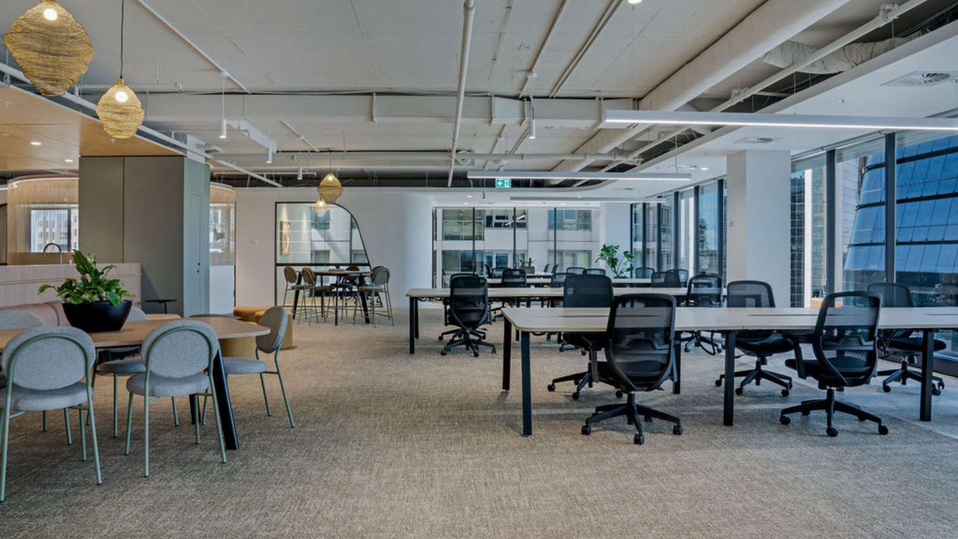 Open-plan commercial office floor with suspended linear LED lights and ergonomic workstations, demonstrating commercial fit-out services in a commercial vs industrial electrician comparison, by Lightspeed Electrical.